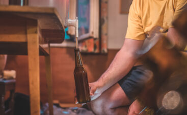 Home craft beer brewery. Final step of pouring a fresh IPA beer into a bottle from fermenter. Hand holding a bottle with home made pale ale beer.